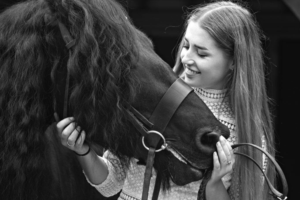 Black and white imagBlack fell pony with a long mane and a girl holding his head in her hands