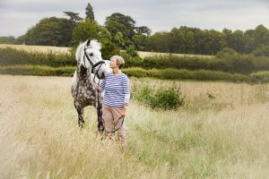 Rider and her grey horse stand in a field of long grass with the Buckinghamshire countryside in the background