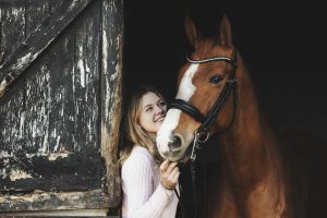 Chesnut horse stands looking out of stable with dressage rider leaning against the stable door