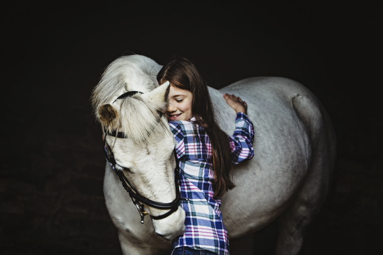 Girl standing in a stable in Northamptonshire with her arms around her grey pony