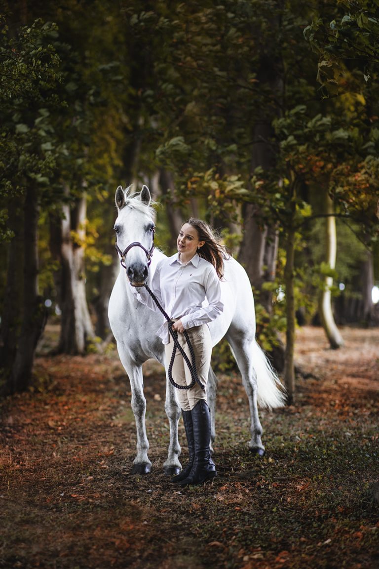 Girls stands with her horse amongst the trees in Buckinghamshire