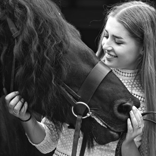 Black and white imagBlack fell pony with a long mane and a girl holding his head in her hands